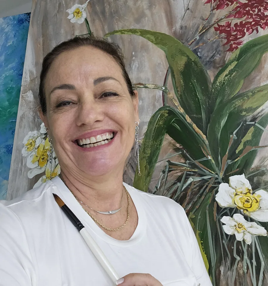 Ane Frenhi sorrindo, com um pincel na mão, em frente a uma tela